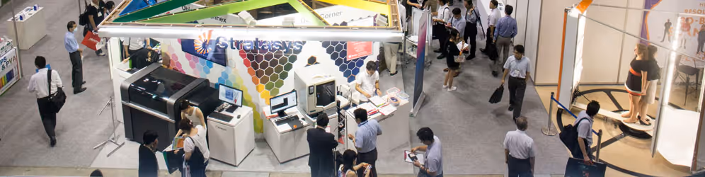 A young woman working in a machine shop. She is looking directly towards the camera, and is surrounded by men.