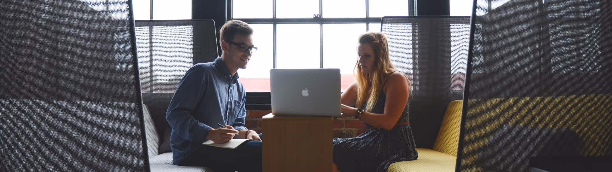 A young woman working in a machine shop. She is looking directly towards the camera, and is surrounded by men.