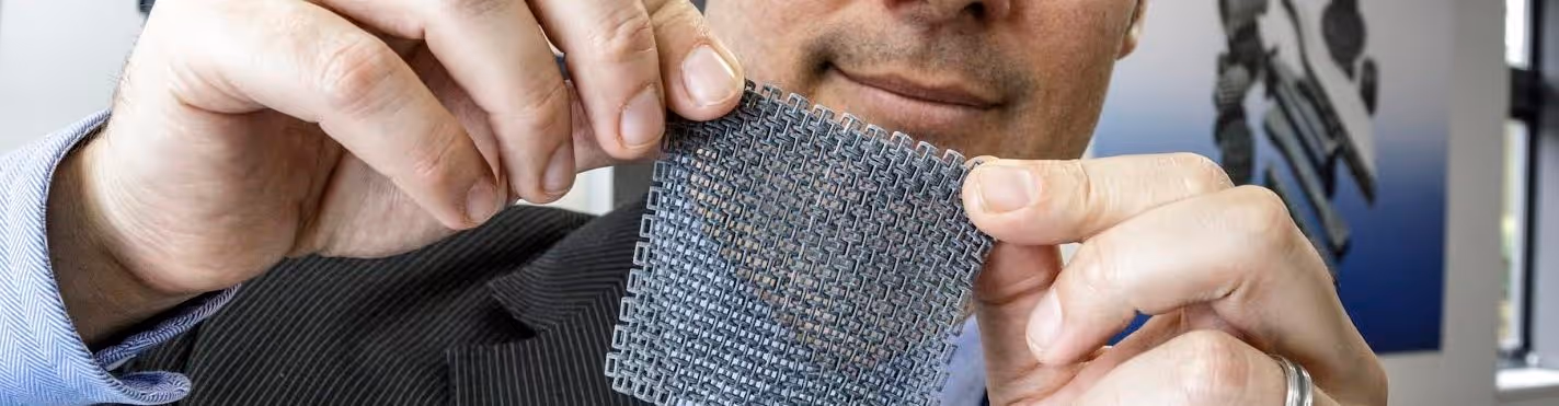 A young woman working in a machine shop. She is looking directly towards the camera, and is surrounded by men.
