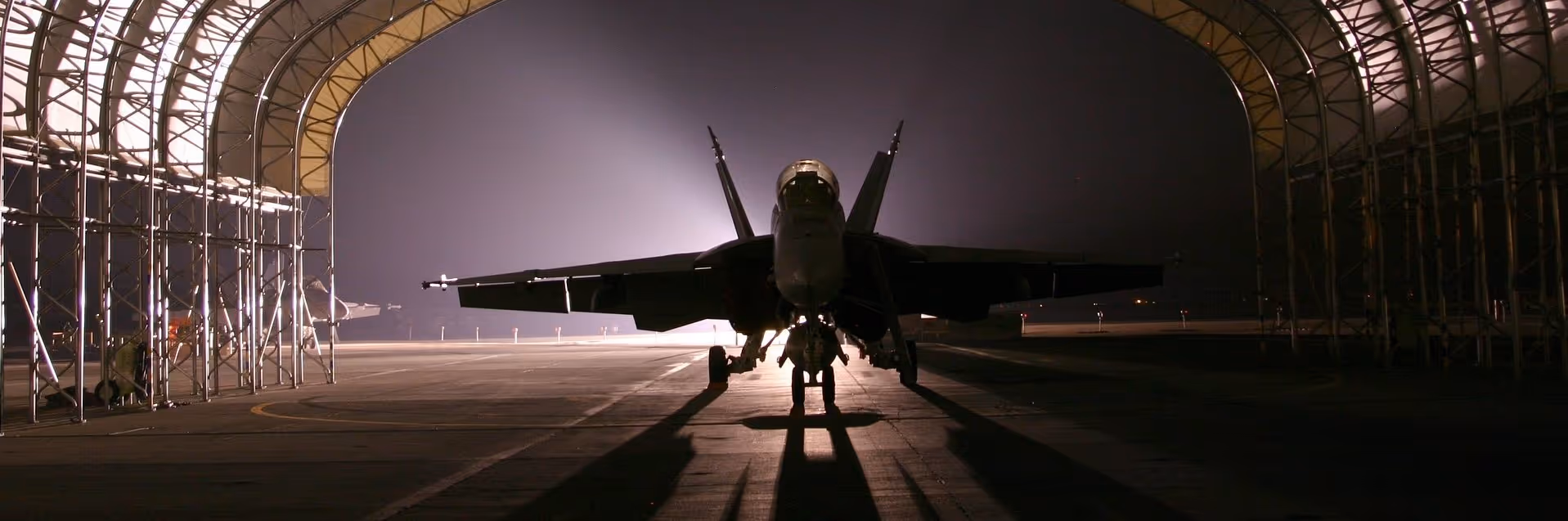 A young woman working in a machine shop. She is looking directly towards the camera, and is surrounded by men.
