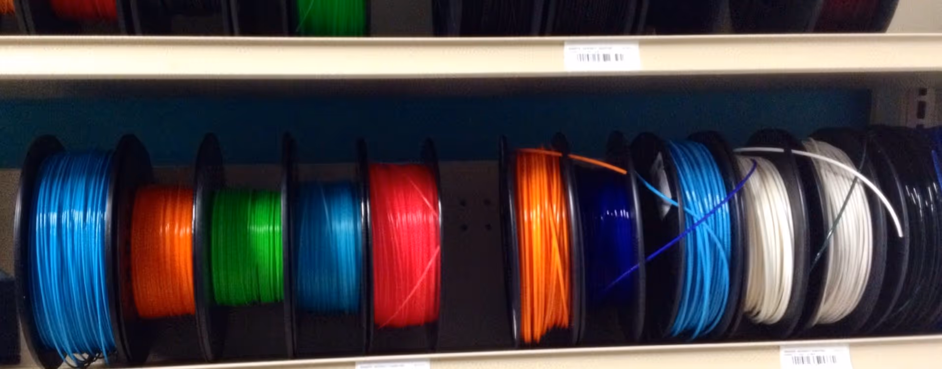 A young woman working in a machine shop. She is looking directly towards the camera, and is surrounded by men.