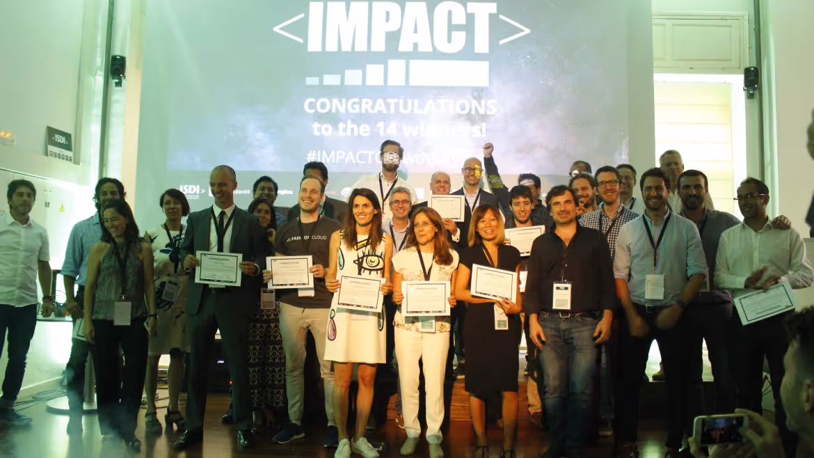 A young woman working in a machine shop. She is looking directly towards the camera, and is surrounded by men.