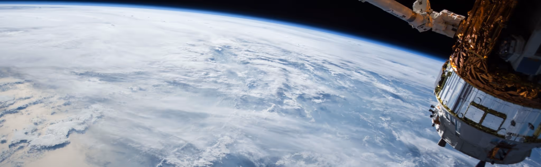 A young woman working in a machine shop. She is looking directly towards the camera, and is surrounded by men.