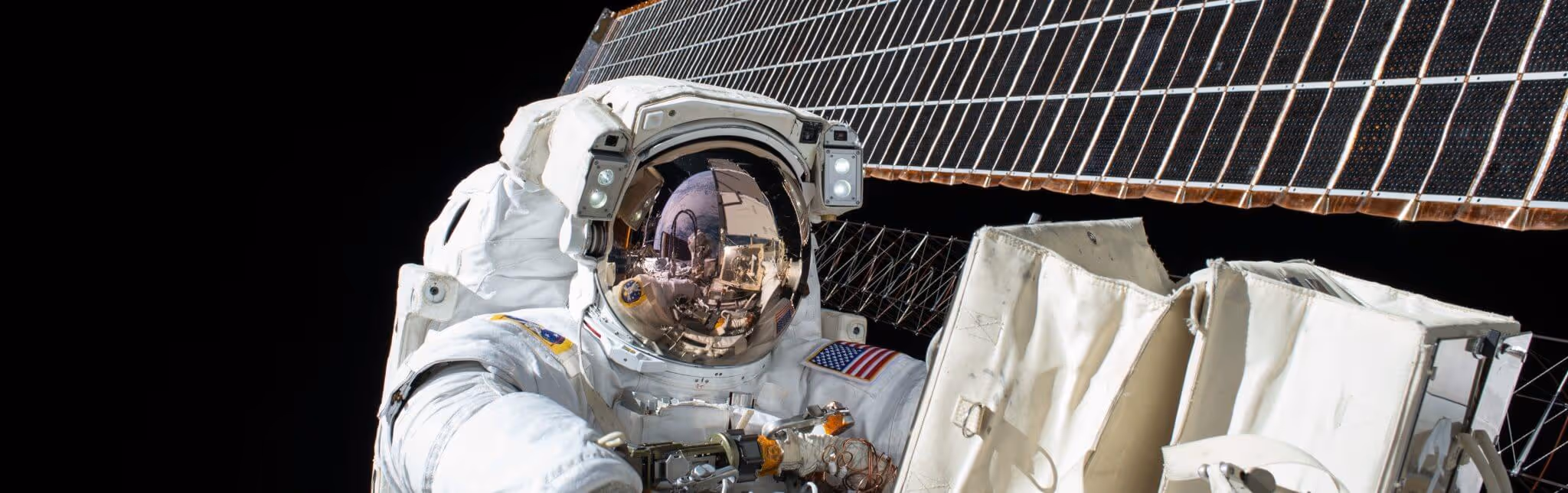 A young woman working in a machine shop. She is looking directly towards the camera, and is surrounded by men.