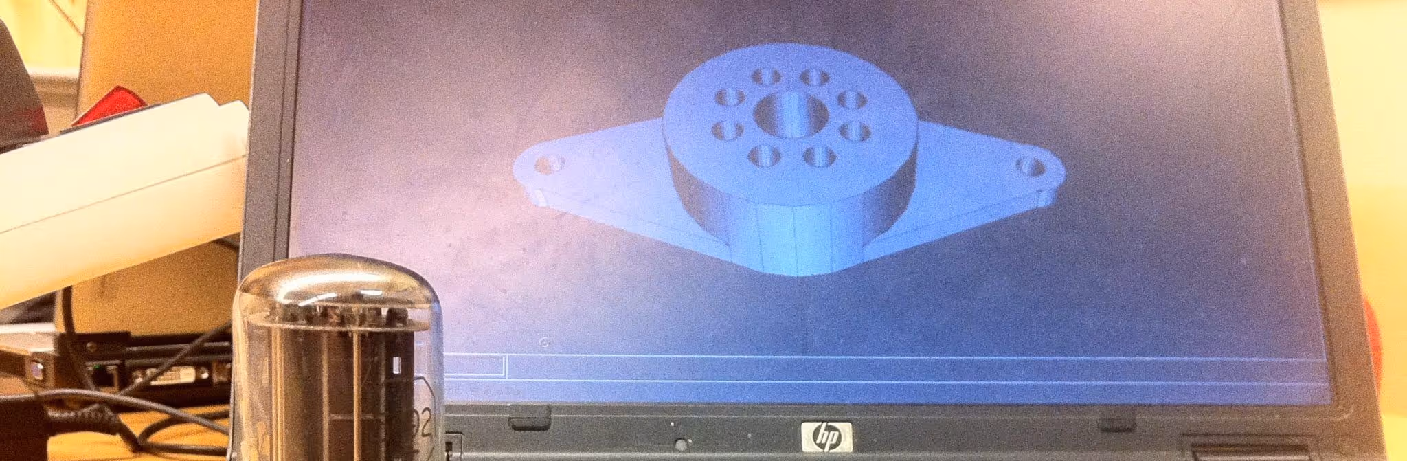 A young woman working in a machine shop. She is looking directly towards the camera, and is surrounded by men.