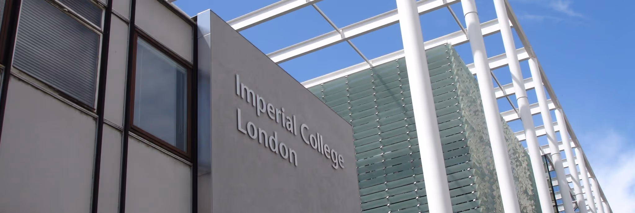 A young woman working in a machine shop. She is looking directly towards the camera, and is surrounded by men.