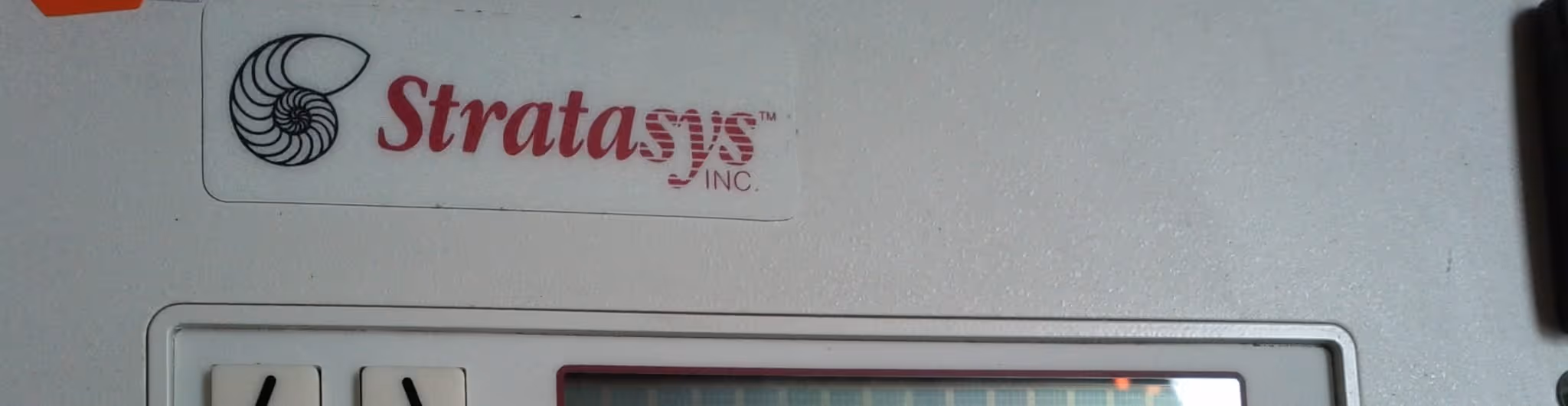 A young woman working in a machine shop. She is looking directly towards the camera, and is surrounded by men.
