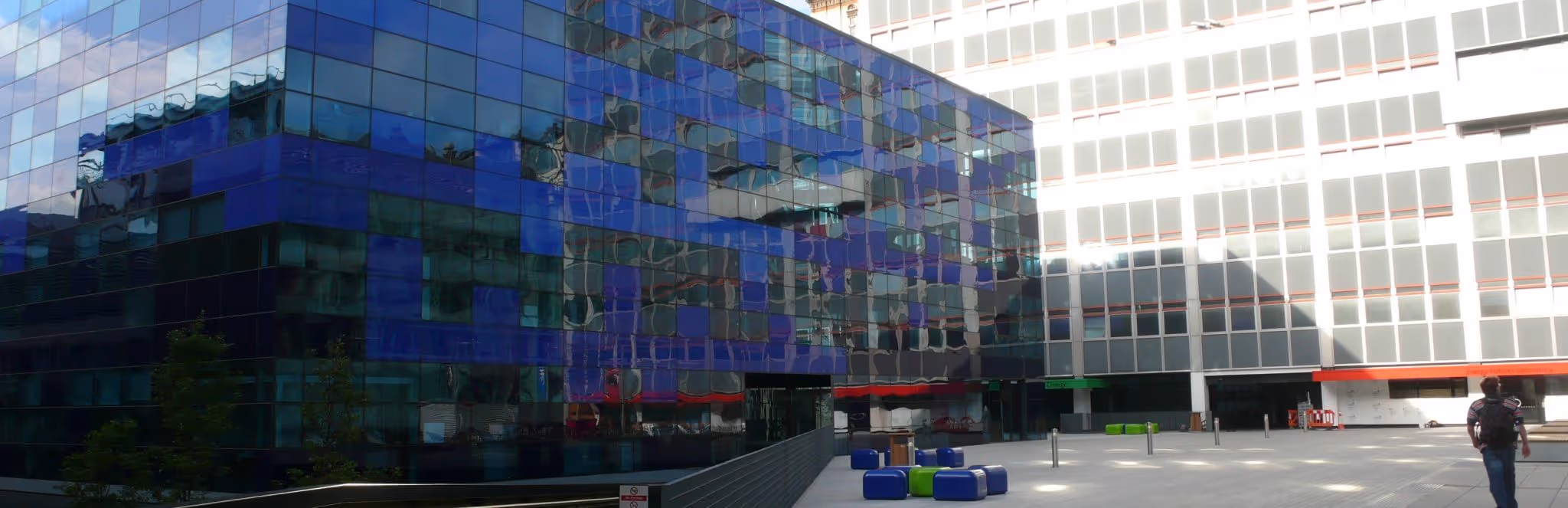 A young woman working in a machine shop. She is looking directly towards the camera, and is surrounded by men.