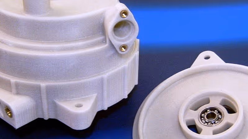 A young woman working in a machine shop. She is looking directly towards the camera, and is surrounded by men.