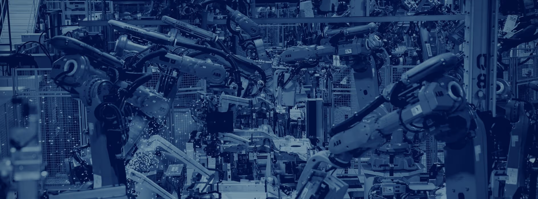 A young woman working in a machine shop. She is looking directly towards the camera, and is surrounded by men.