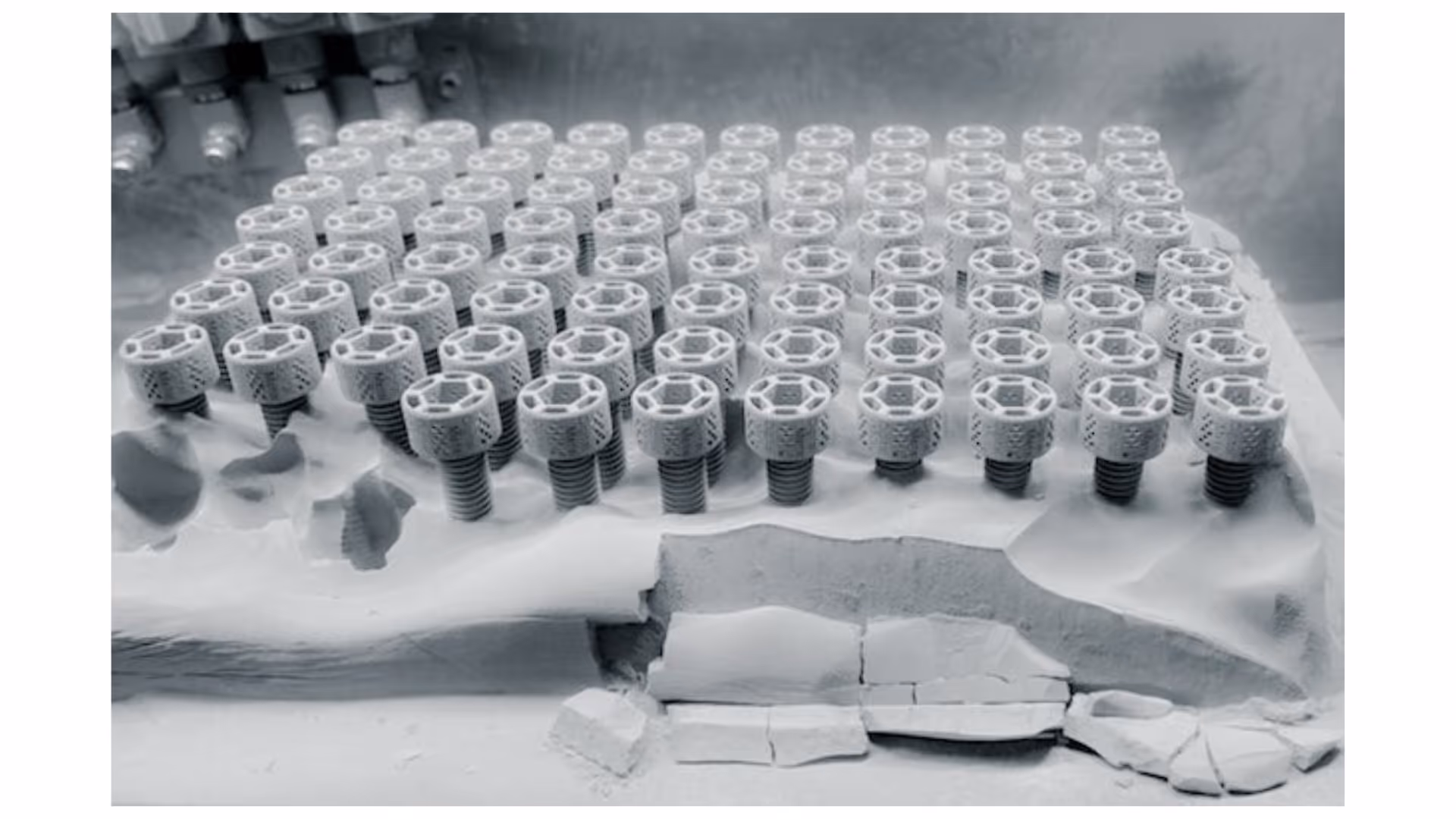 A young woman working in a machine shop. She is looking directly towards the camera, and is surrounded by men.