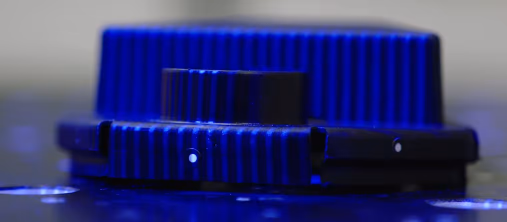A young woman working in a machine shop. She is looking directly towards the camera, and is surrounded by men.