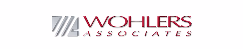 A young woman working in a machine shop. She is looking directly towards the camera, and is surrounded by men.