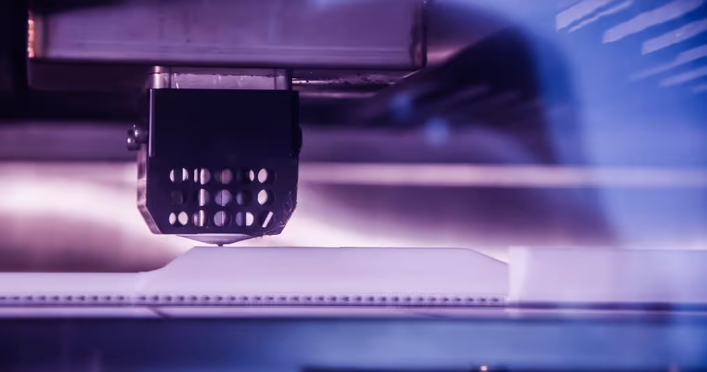 A young woman working in a machine shop. She is looking directly towards the camera, and is surrounded by men.