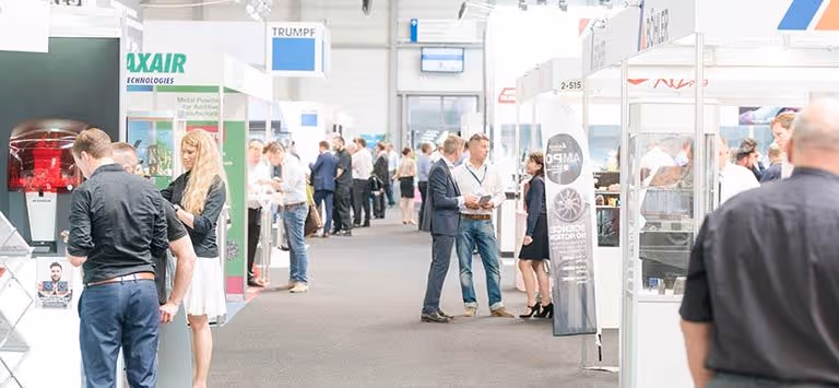 A young woman working in a machine shop. She is looking directly towards the camera, and is surrounded by men.