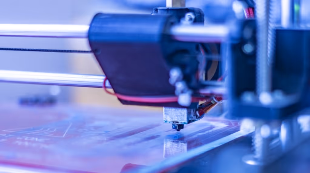 A young woman working in a machine shop. She is looking directly towards the camera, and is surrounded by men.