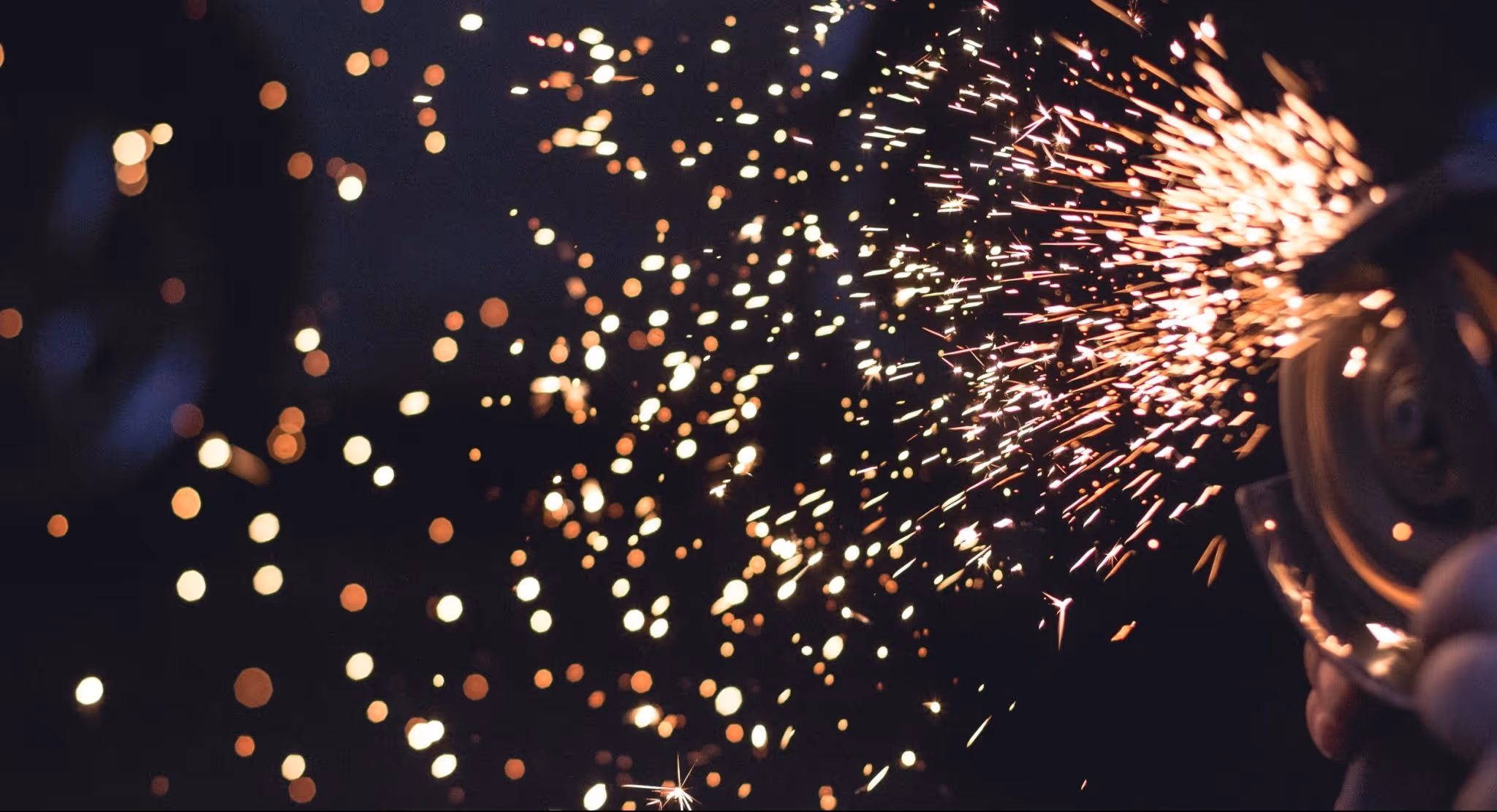A young woman working in a machine shop. She is looking directly towards the camera, and is surrounded by men.