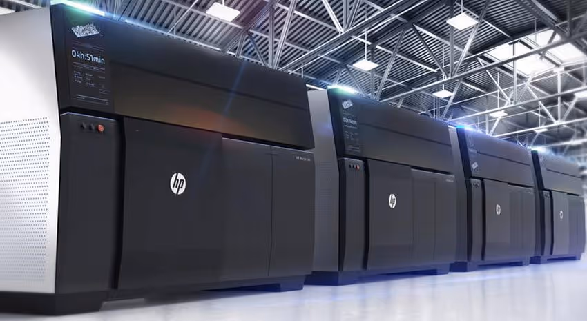 A young woman working in a machine shop. She is looking directly towards the camera, and is surrounded by men.