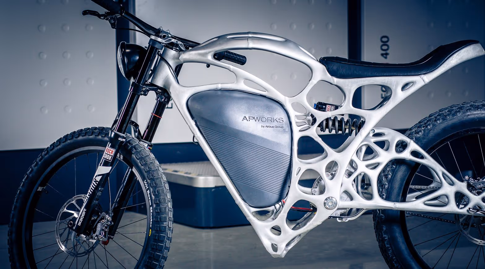 A young woman working in a machine shop. She is looking directly towards the camera, and is surrounded by men.