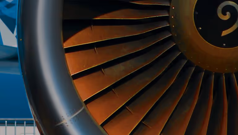 A young woman working in a machine shop. She is looking directly towards the camera, and is surrounded by men.
