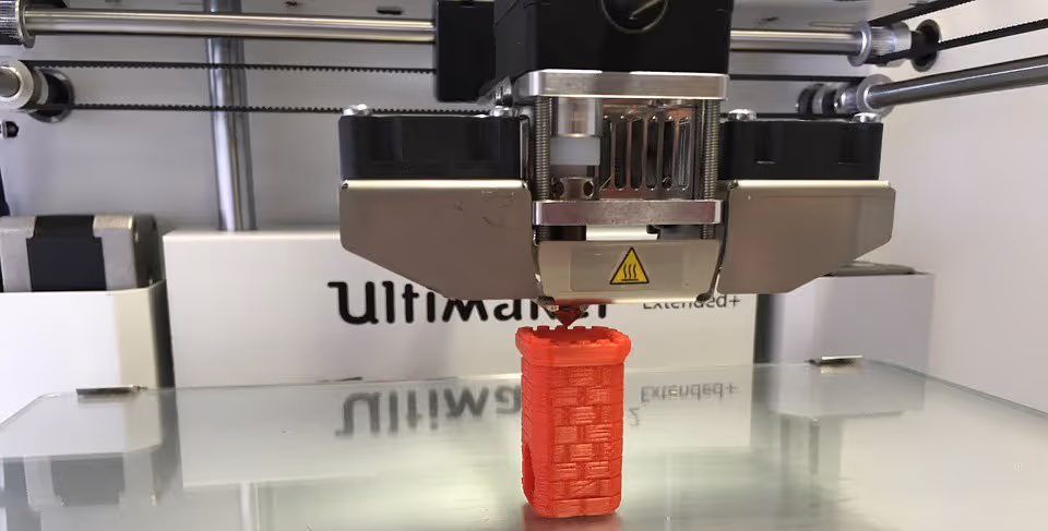 A young woman working in a machine shop. She is looking directly towards the camera, and is surrounded by men.