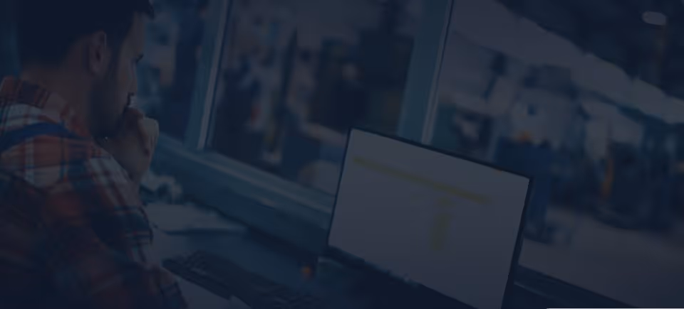 A young woman working in a machine shop. She is looking directly towards the camera, and is surrounded by men.