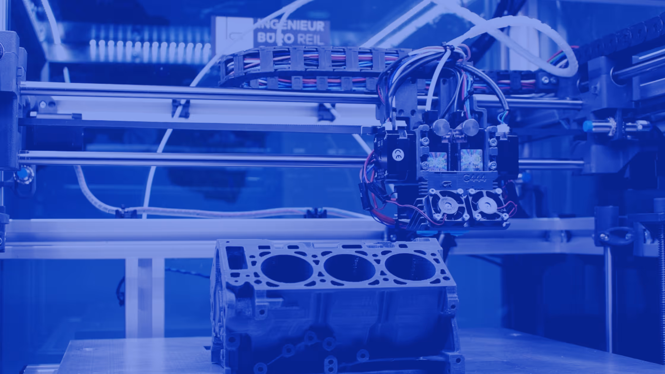 A young woman working in a machine shop. She is looking directly towards the camera, and is surrounded by men.