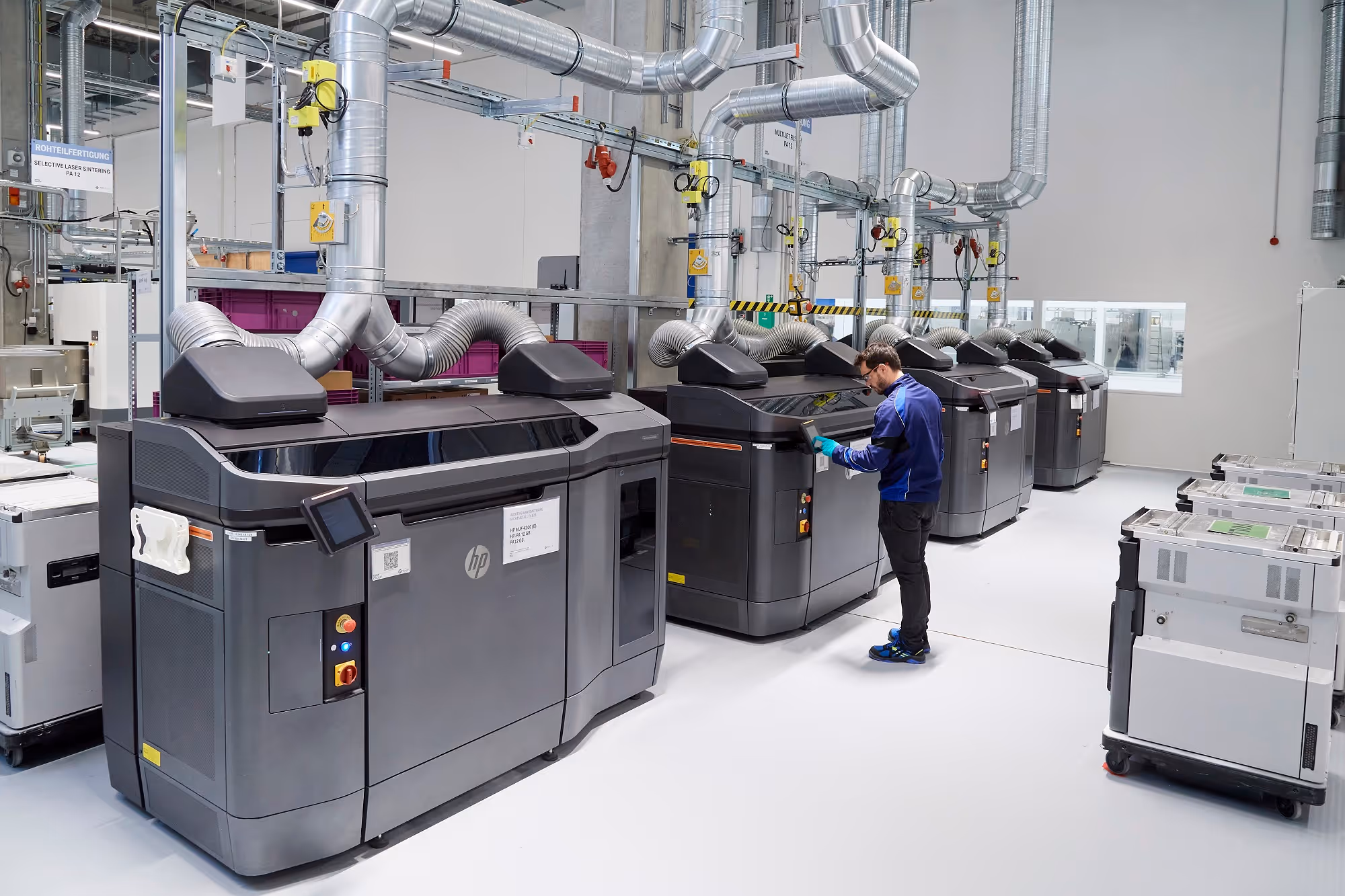 A young woman working in a machine shop. She is looking directly towards the camera, and is surrounded by men.