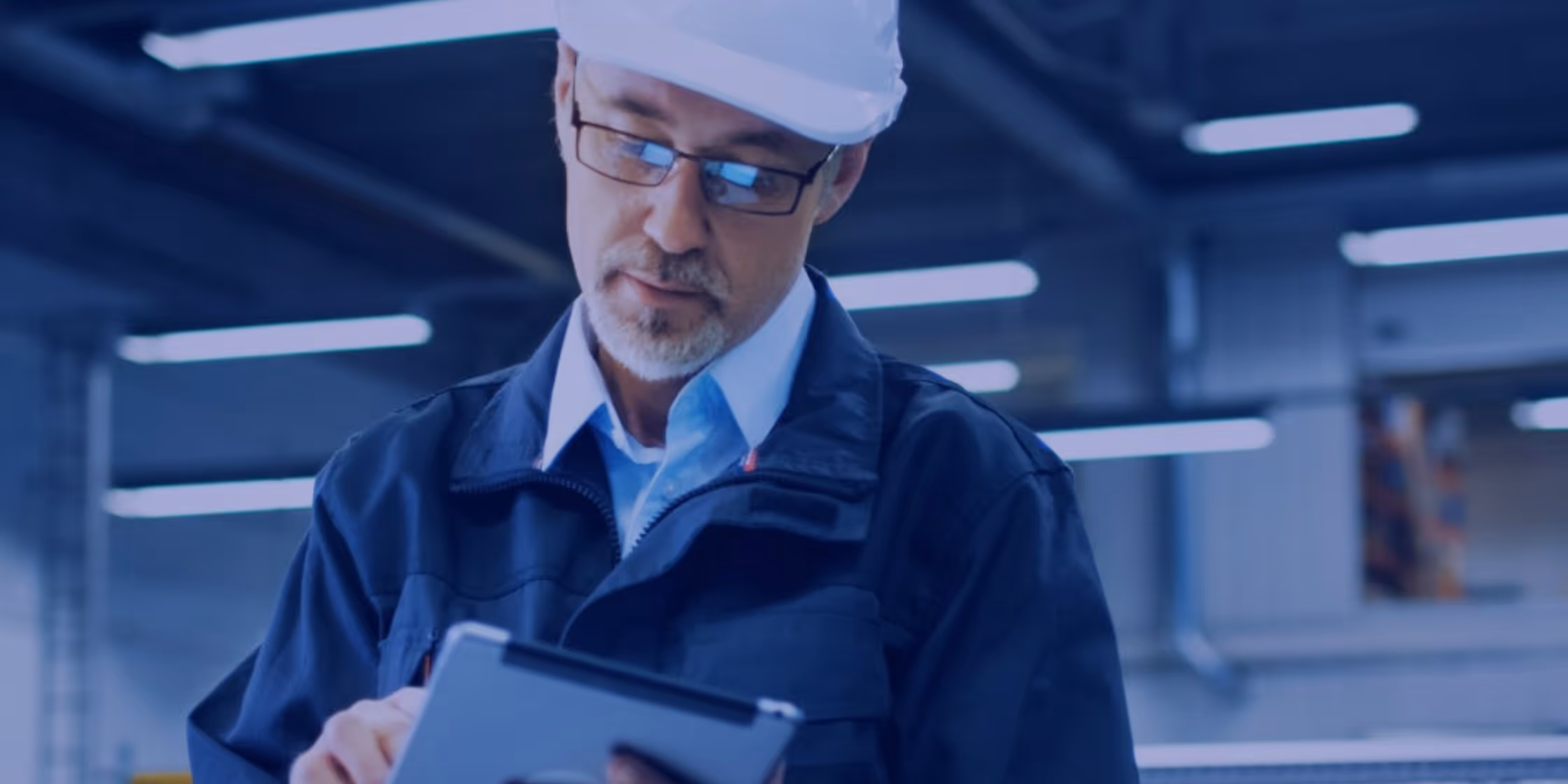 A young woman working in a machine shop. She is looking directly towards the camera, and is surrounded by men.
