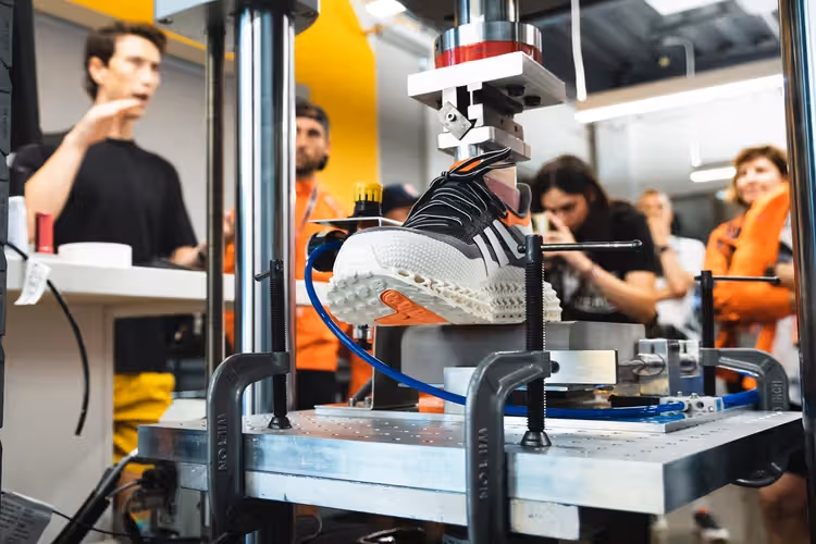 A young woman working in a machine shop. She is looking directly towards the camera, and is surrounded by men.