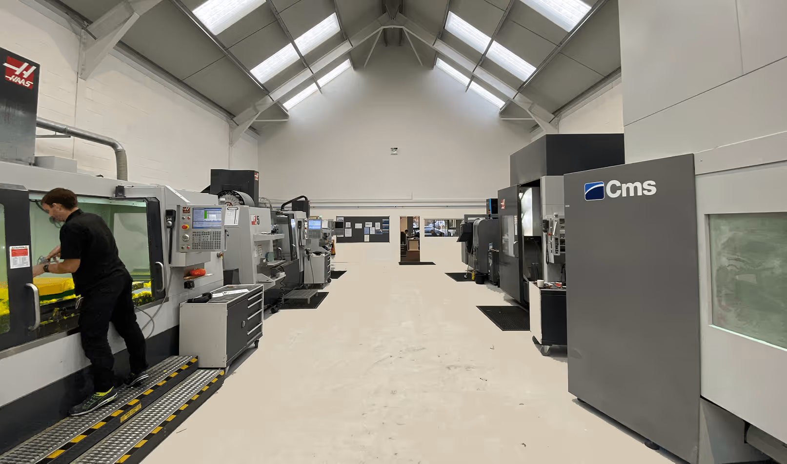 A young woman working in a machine shop. She is looking directly towards the camera, and is surrounded by men.