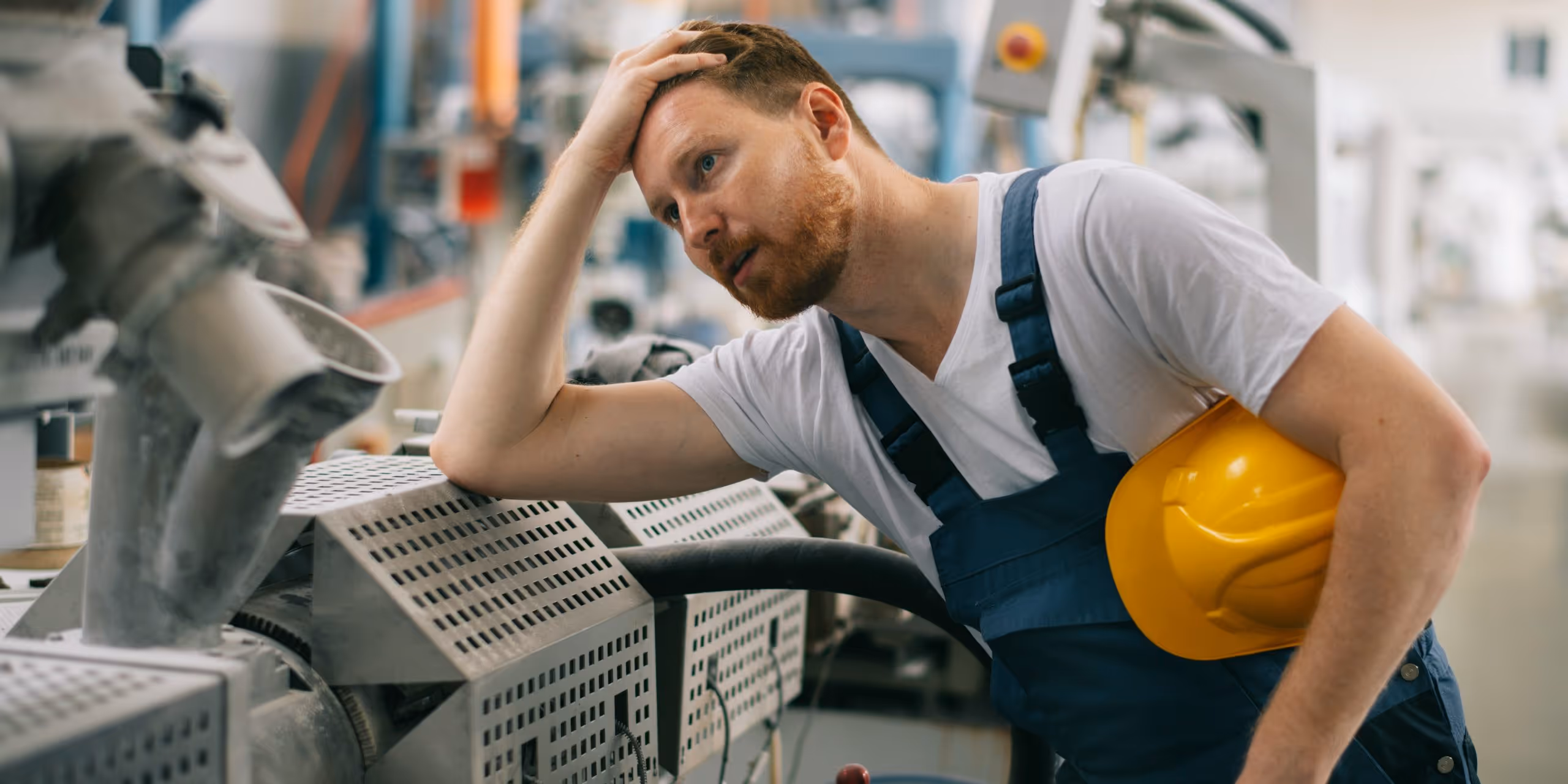 A young woman working in a machine shop. She is looking directly towards the camera, and is surrounded by men.