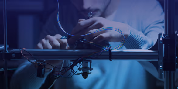 A young woman working in a machine shop. She is looking directly towards the camera, and is surrounded by men.