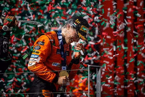 A young woman working in a machine shop. She is looking directly towards the camera, and is surrounded by men.