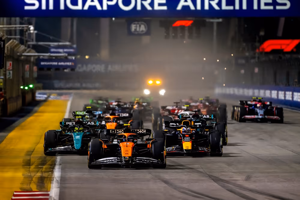 A young woman working in a machine shop. She is looking directly towards the camera, and is surrounded by men.