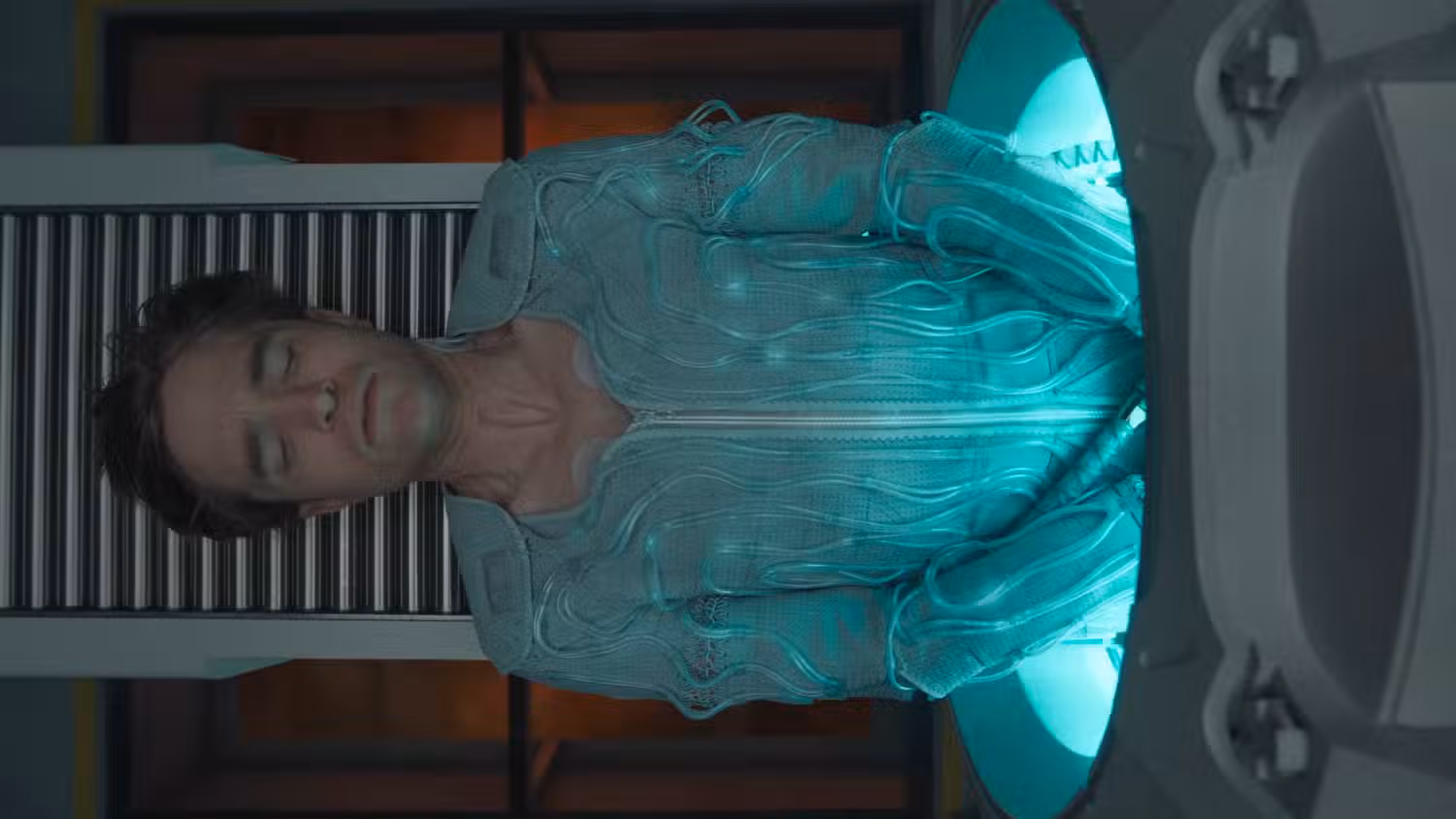 A young woman working in a machine shop. She is looking directly towards the camera, and is surrounded by men.