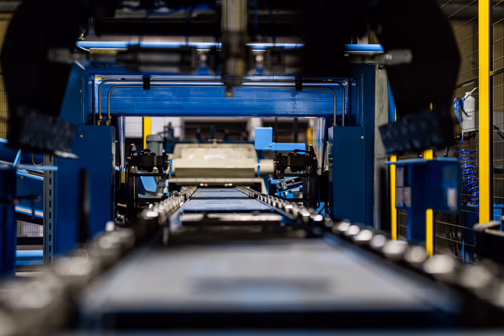 A young woman working in a machine shop. She is looking directly towards the camera, and is surrounded by men.