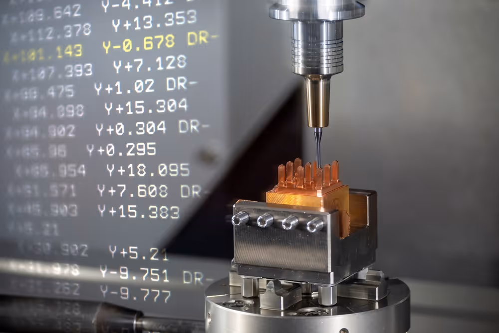 A young woman working in a machine shop. She is looking directly towards the camera, and is surrounded by men.