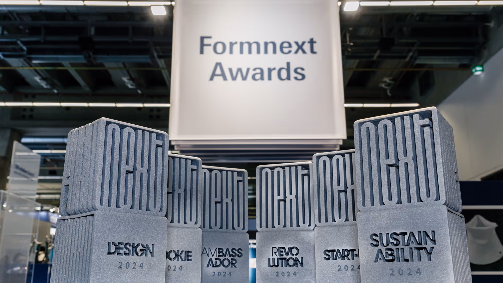 A young woman working in a machine shop. She is looking directly towards the camera, and is surrounded by men.