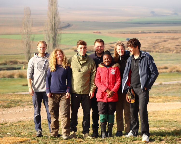 Group picture of young people standing on a field with trees in the background