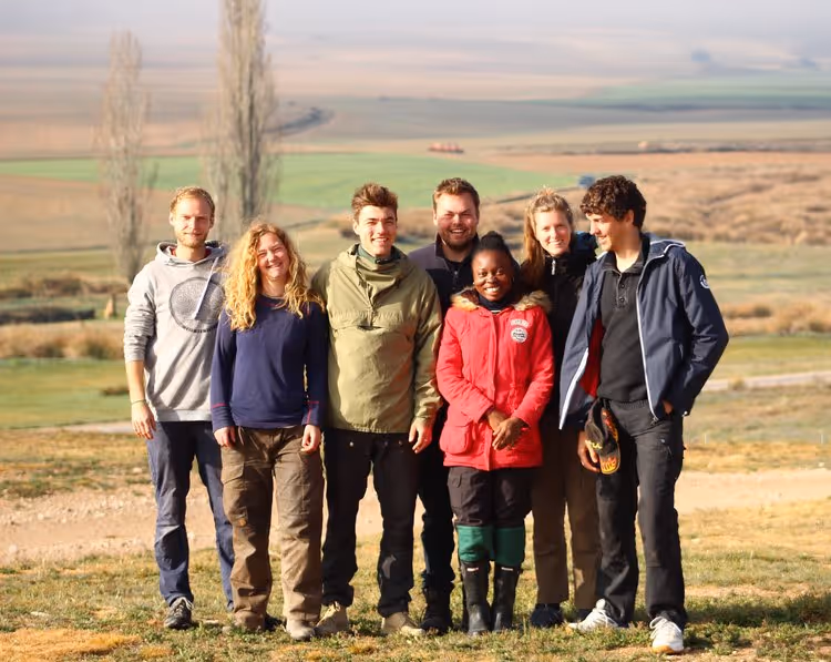 Group picture of young people standing on a field with trees in the background