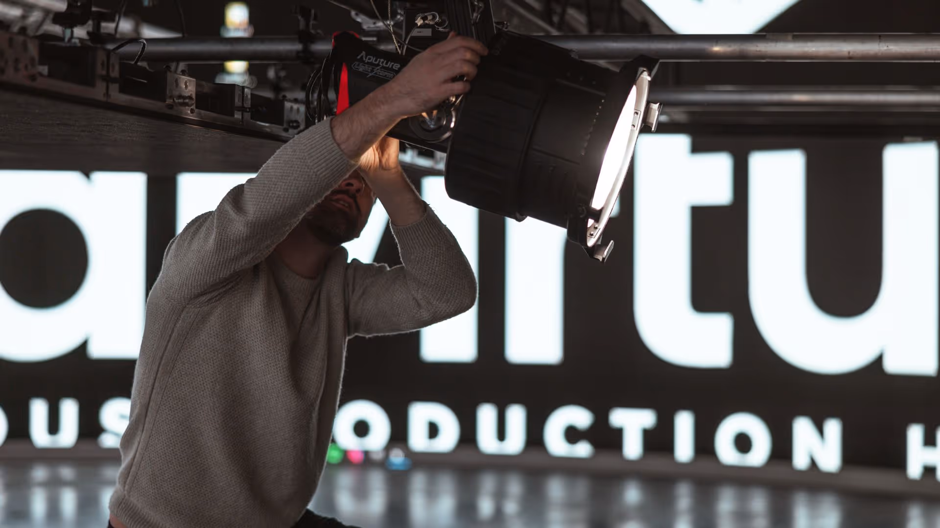Un membre de l'équipe de production de L'Imagerie Films règle une lampe Aputure lors d'une installation de production vidéo professionnelle.