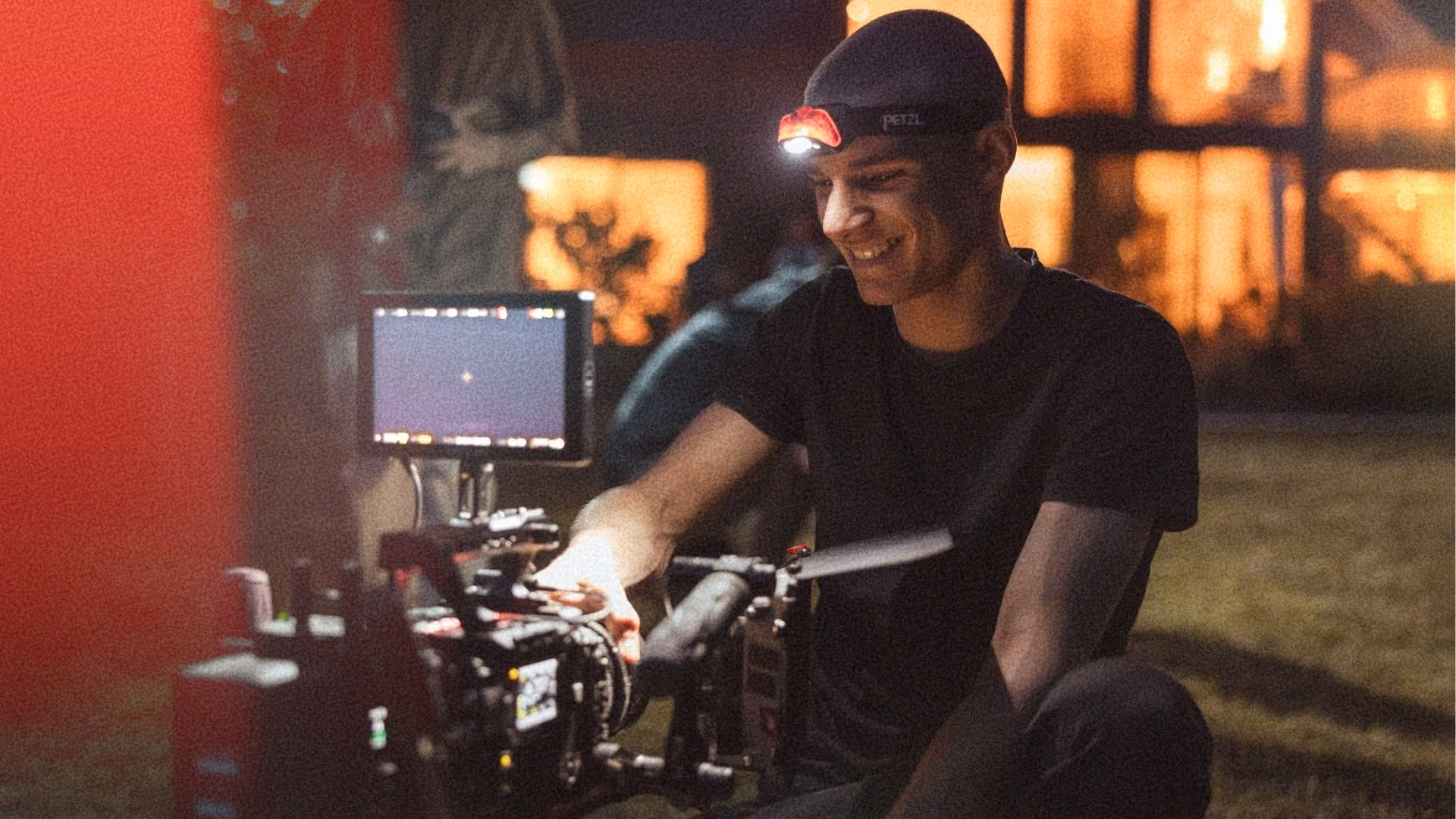 Camera operator from L'Imagerie Films adjusting a cinema camera rig during a nighttime brand film production.
