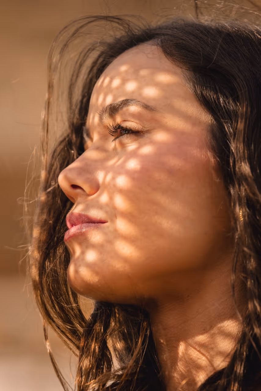 Close-up portrait of a woman with patterned sunlight across her face in a cinematic brand film production.
