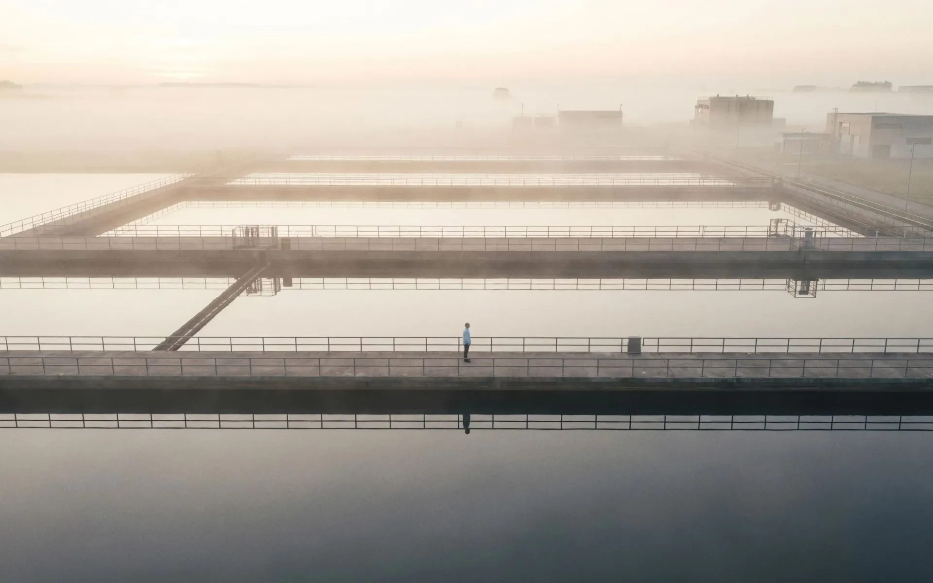 Vue aérienne de bassins d'eau aux formes géométriques dans un paysage industriel embrumé, issue d'une production de L'Imagerie Films.