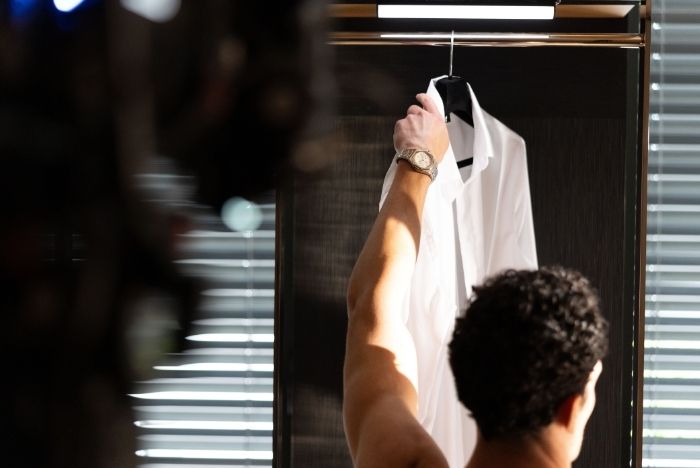 Person reaching for a white shirt while wearing a wristwatch during luxury brand film production.