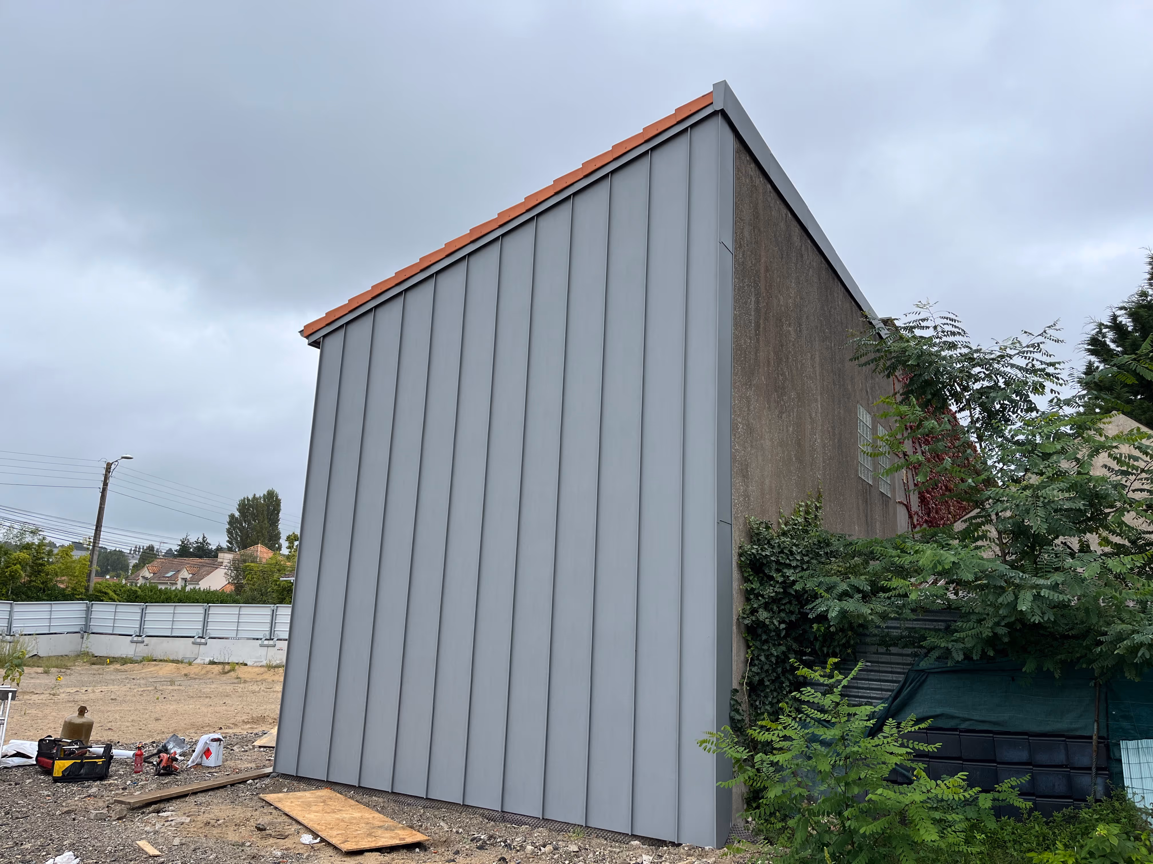 Bardage métallique gris sur un bâtiment avec finition en zinc et bordure de toit en tuiles