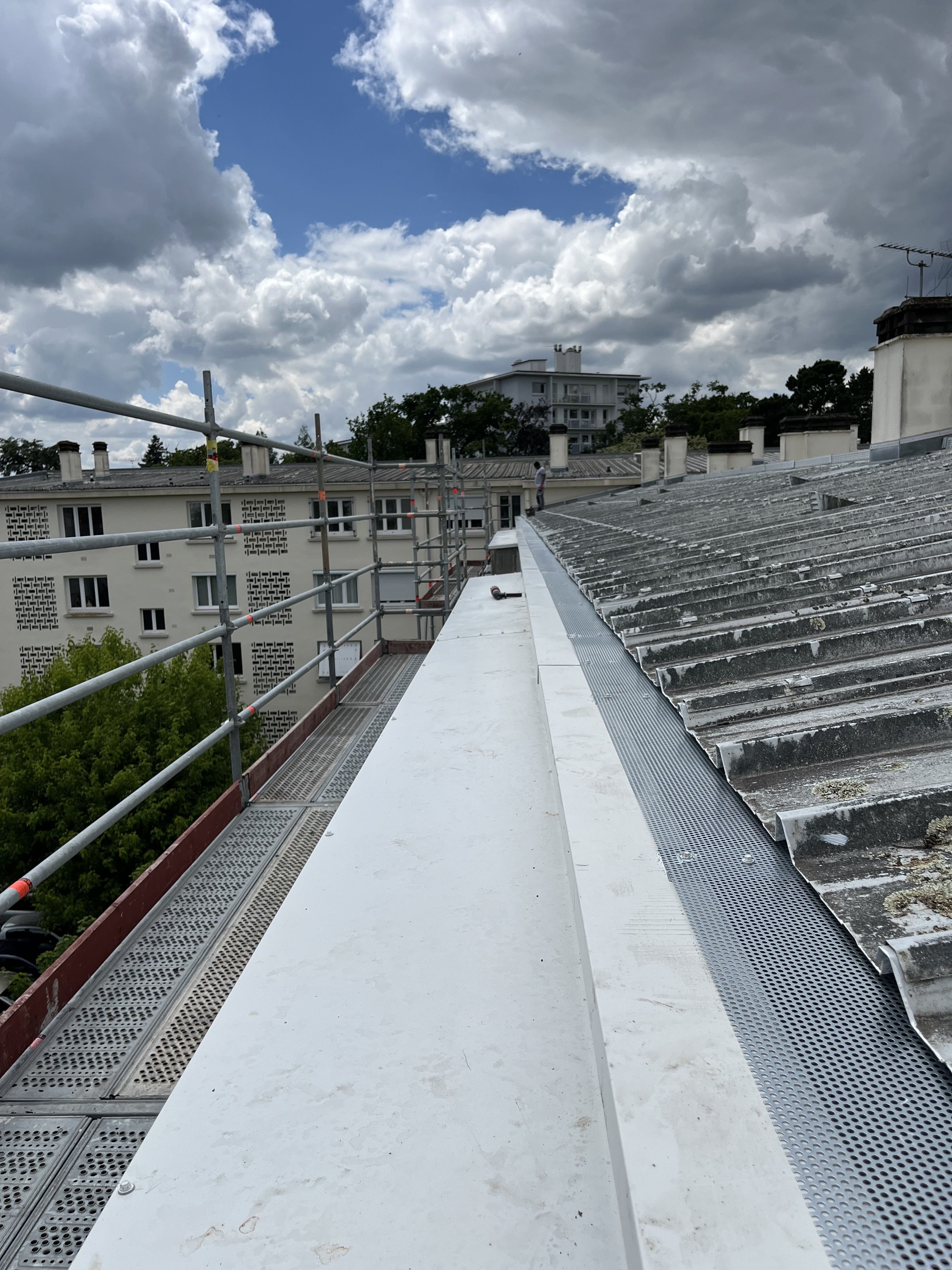 Toit d'un bâtiment avec des plaques métalliques ondulées, un échafaudage sur le côté et un ciel nuageux en arrière-plan.