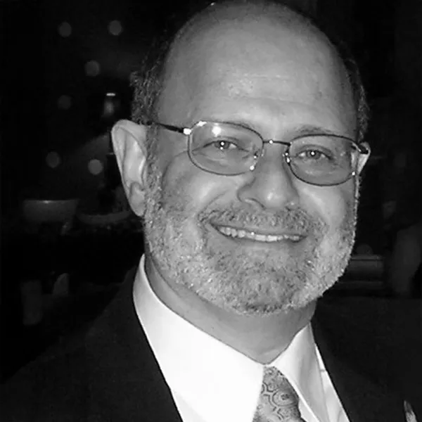 Alan Lewis, Cytonics team member, smiling in a dark suit and patterned tie with wire-frame glasses