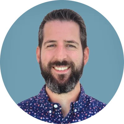 Smiling man with dark hair and beard wearing a patterned blue shirt